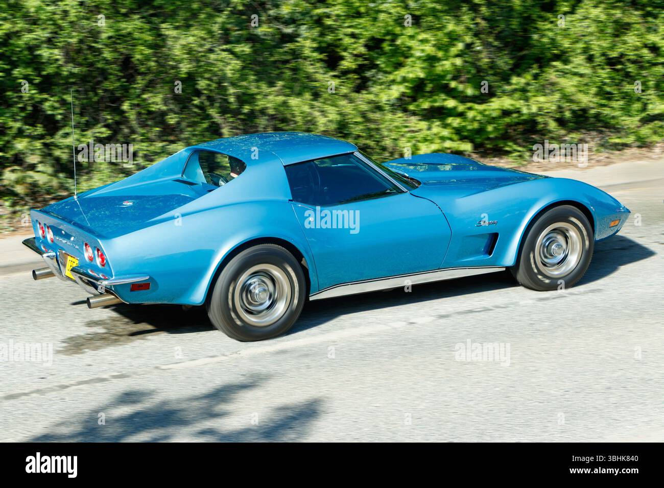 Bleu classique des années 1970 vintage chevrolet corvette Stingray voiture de sport conduisant sur une route ensoleillée avec un feuillage vert luxuriant en arrière-plan Banque D'Images