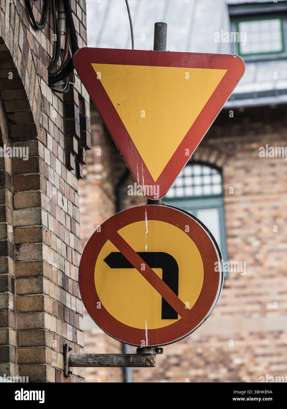 Deux panneaux de signalisation routière sont bien en vue sur un bâtiment en Suède. Un panneau indique aux conducteurs de céder, tandis que l'autre interdit les virages à gauche. L'urbain Banque D'Images