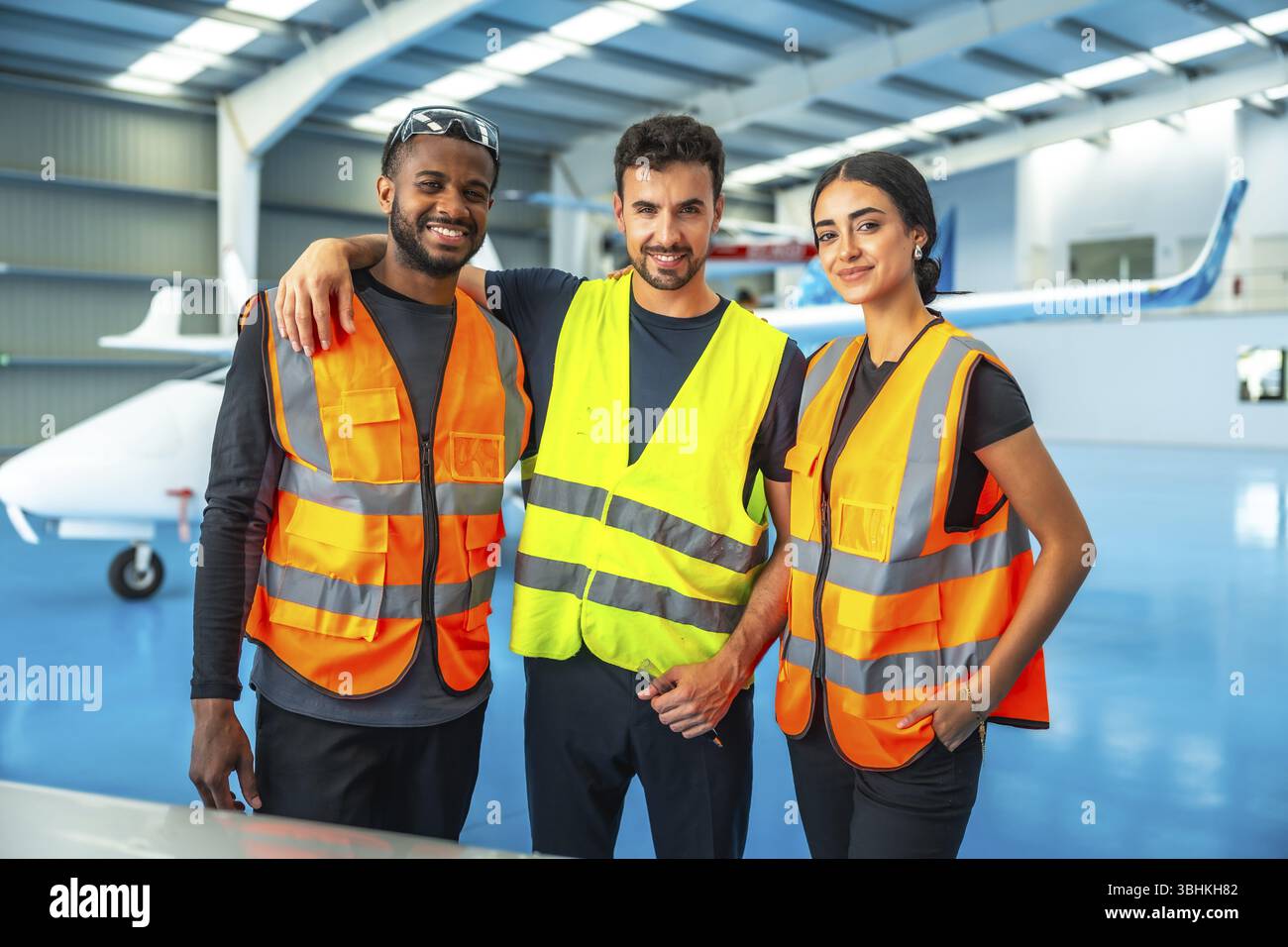 Trois techniciens d'entretien d'aéronefs portant des gilets haute visibilité se tiennent ensemble dans un hangar d'avion, incarnant le travail d'équipe et le professionnalisme dans un Banque D'Images