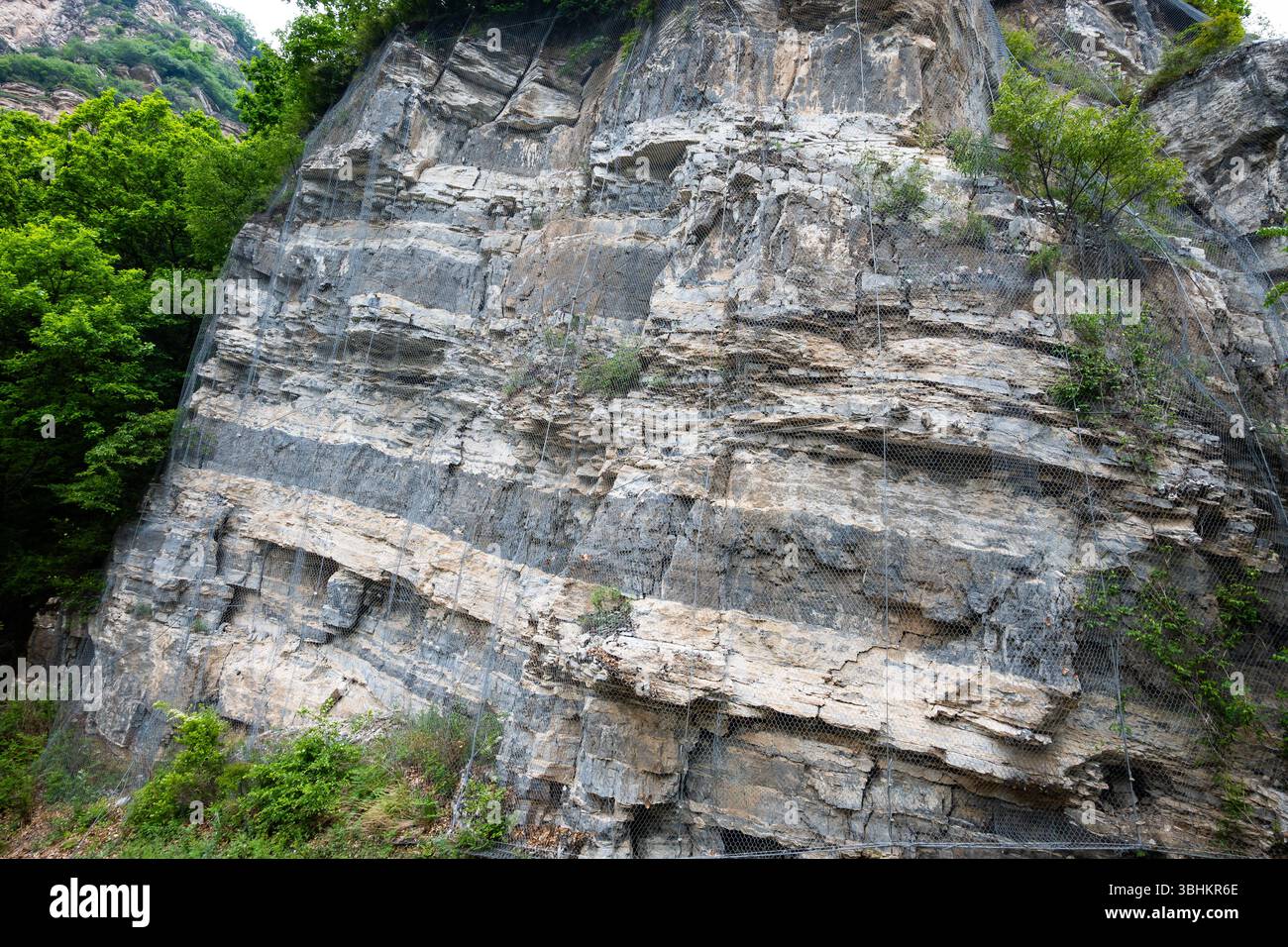 Coupe de route rocheuse sécurisée par un treillis métallique contre les chutes de roches. Pékin, Chine. Banque D'Images