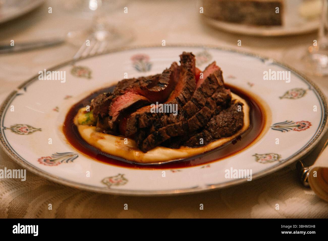 Un plat de bœuf magnifiquement présenté se compose de viande tendre sur un lit de purée de pommes de terre crémeuse, arrosé d'une sauce riche. Banque D'Images