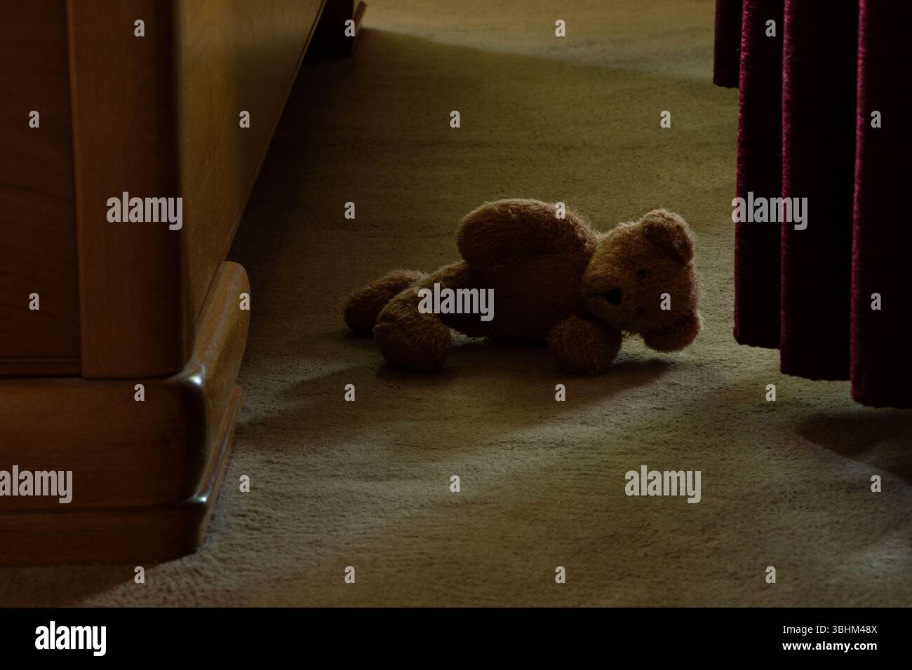 Un ours en peluche repose sur le sol dans la chambre sur le tapis dans l'obscurité, un jouet abandonné seul Banque D'Images