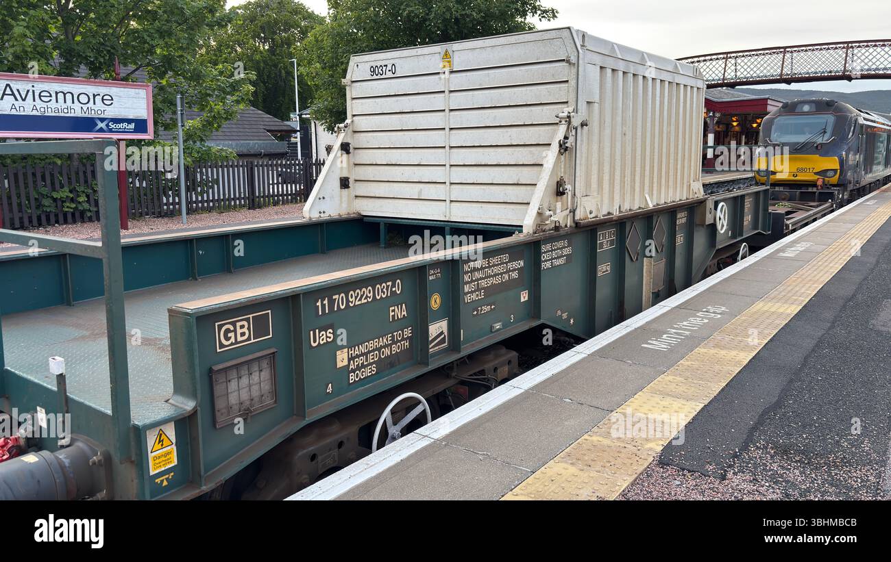 Un train de marchandises passe devant la gare d'Aviemore, transportant des marchandises à travers les Highlands, illustrant le transport rural vital et l'industrie. Banque D'Images