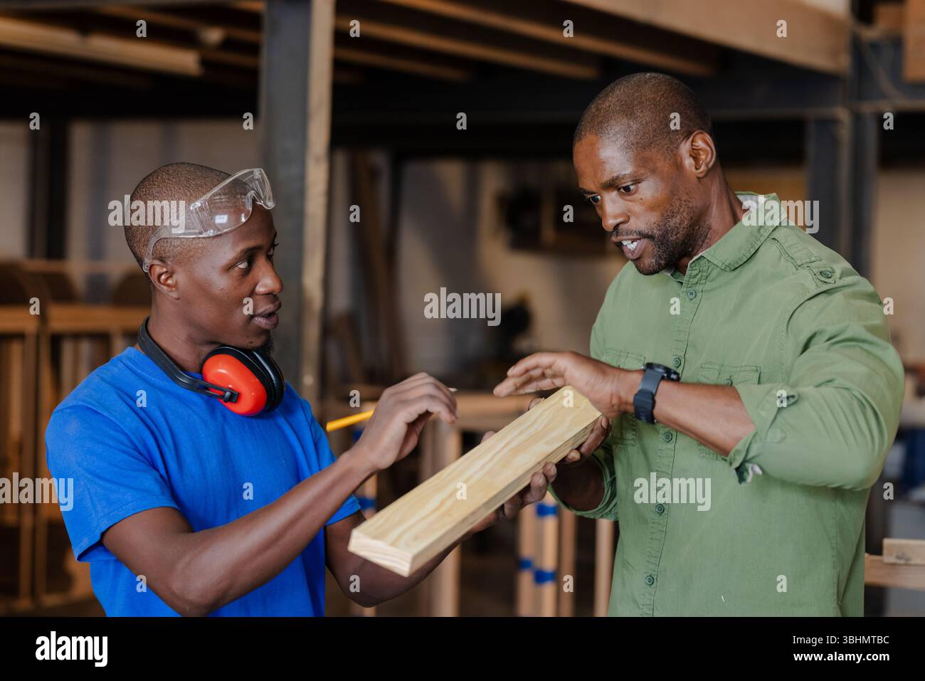 Collègues afro-américains mesurant la planche de bois dans un magasin de menuiserie avec des lunettes de crayon cache-oreilles Banque D'Images