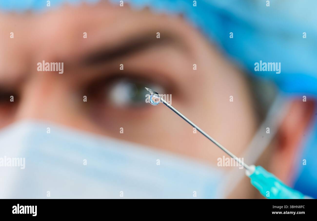 Goutte de médicament sur l'extrémité de l'aiguille d'injection médicale. Mise au point sélective. Docteur en masque médical avec seringue pour injection. Vaccination. Gros plan de la goutte Banque D'Images
