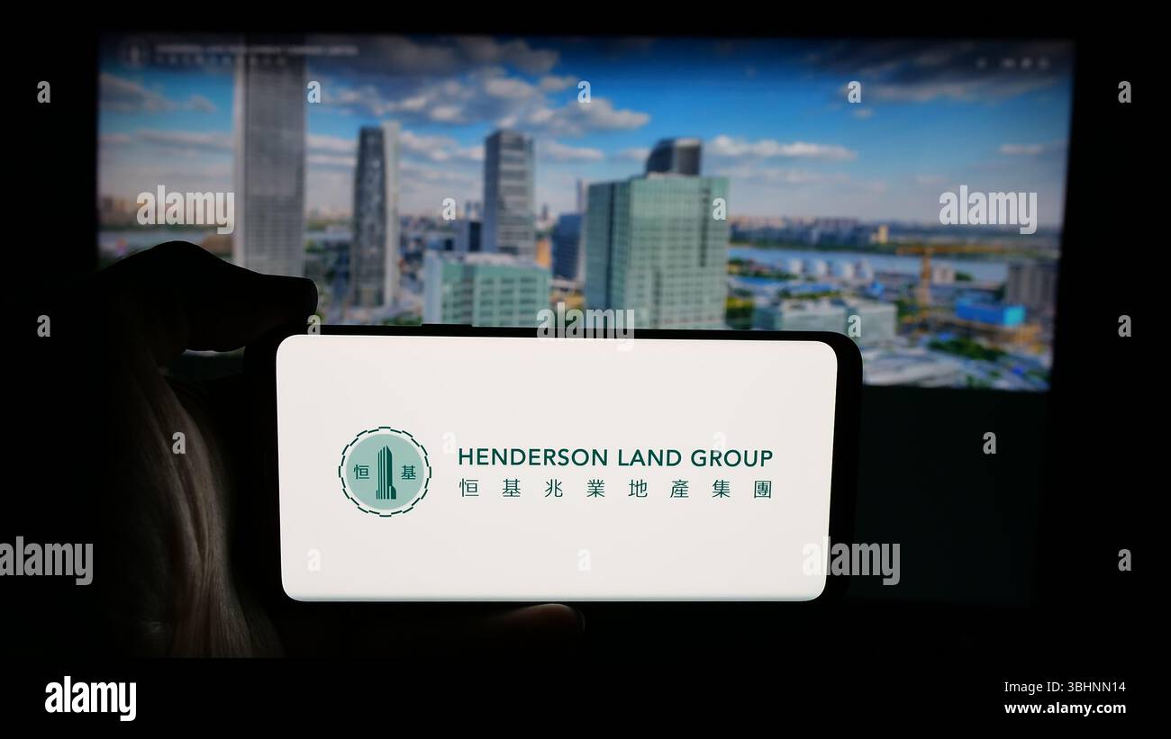 Stuttgart, Allemagne - 03-14-2025 : personne tenant un téléphone portable avec le logo de la société Henderson Land Development Co. Ltd sur l'écran devant la page web. Banque D'Images Stuttgart, Allemagne - 03-14-2025 : personne tenant un téléphone portable avec le logo de la société Henderson Land Development Co. Ltd sur l'écran devant la page web. Banque D'Images