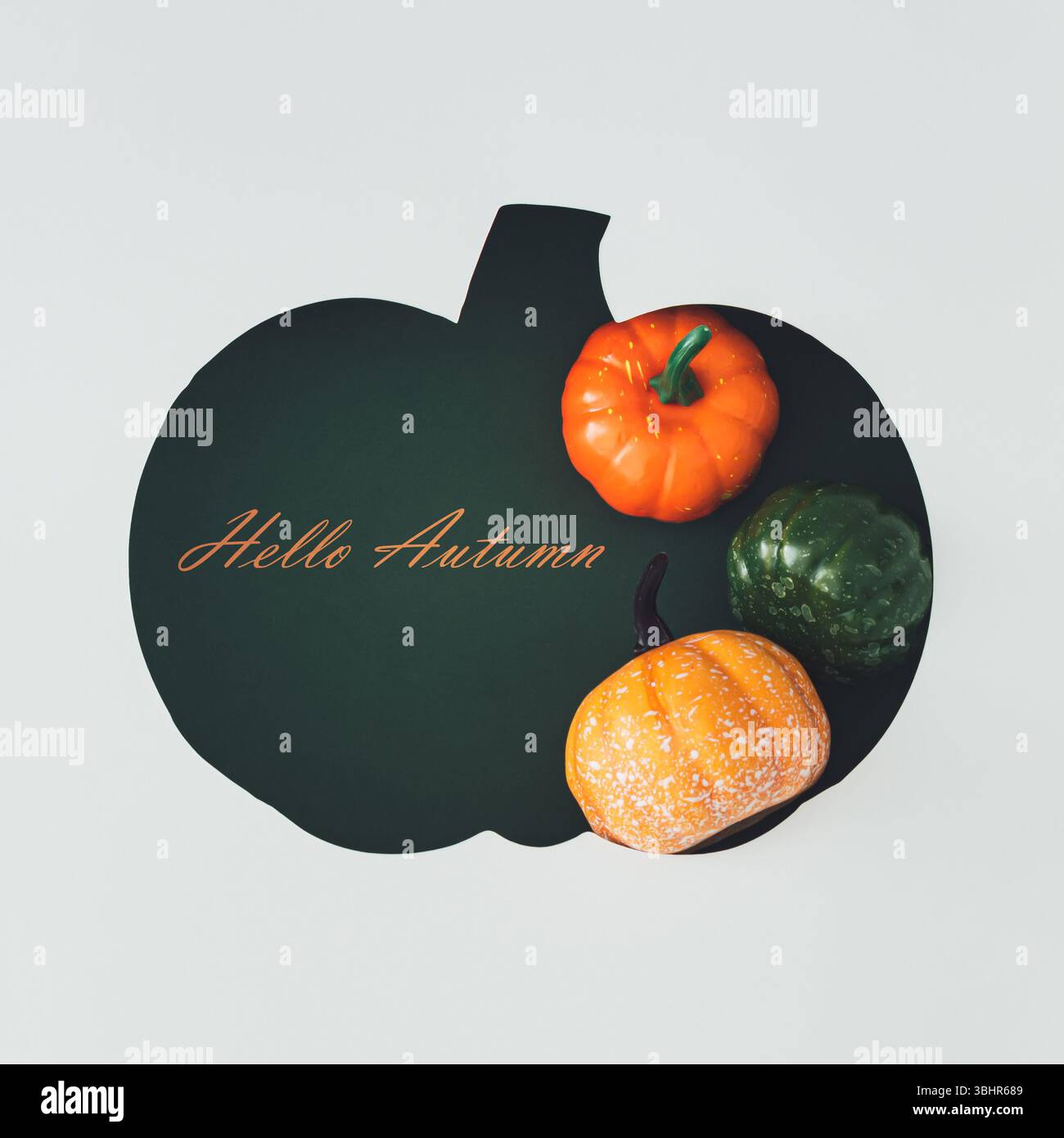 Pose à plat créative de citrouilles décoratives avec texte Hello Autumn visible à travers un espace en forme de citrouille. Concept saisonnier confortable pour les arrière-plans d'automne. Banque D'Images
