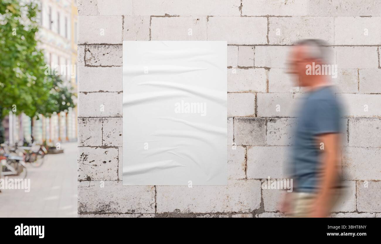 Homme marchant devant la maquette d'affiche blanche sur le mur de pierre polie près de la promenade de la ville. Idéal pour les maquettes d'affiche, de marque et de campagne Banque D'Images