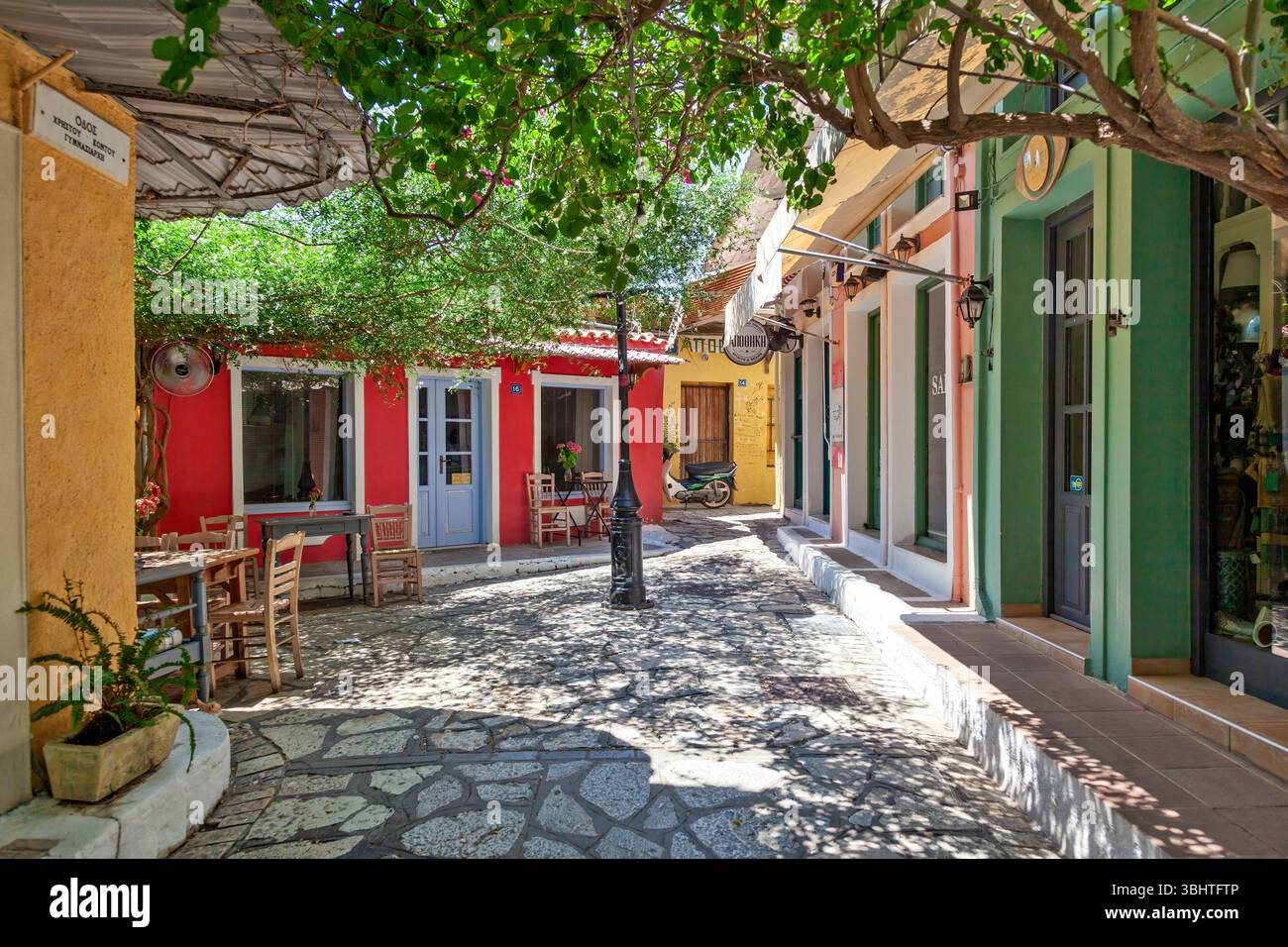 Ruelle colorée à Preveza, en Grèce, avec des tavernes traditionnelles, chemin pavé ombragé et charme méditerranéen dans un cadre paisible et ensoleillé. Banque D'Images