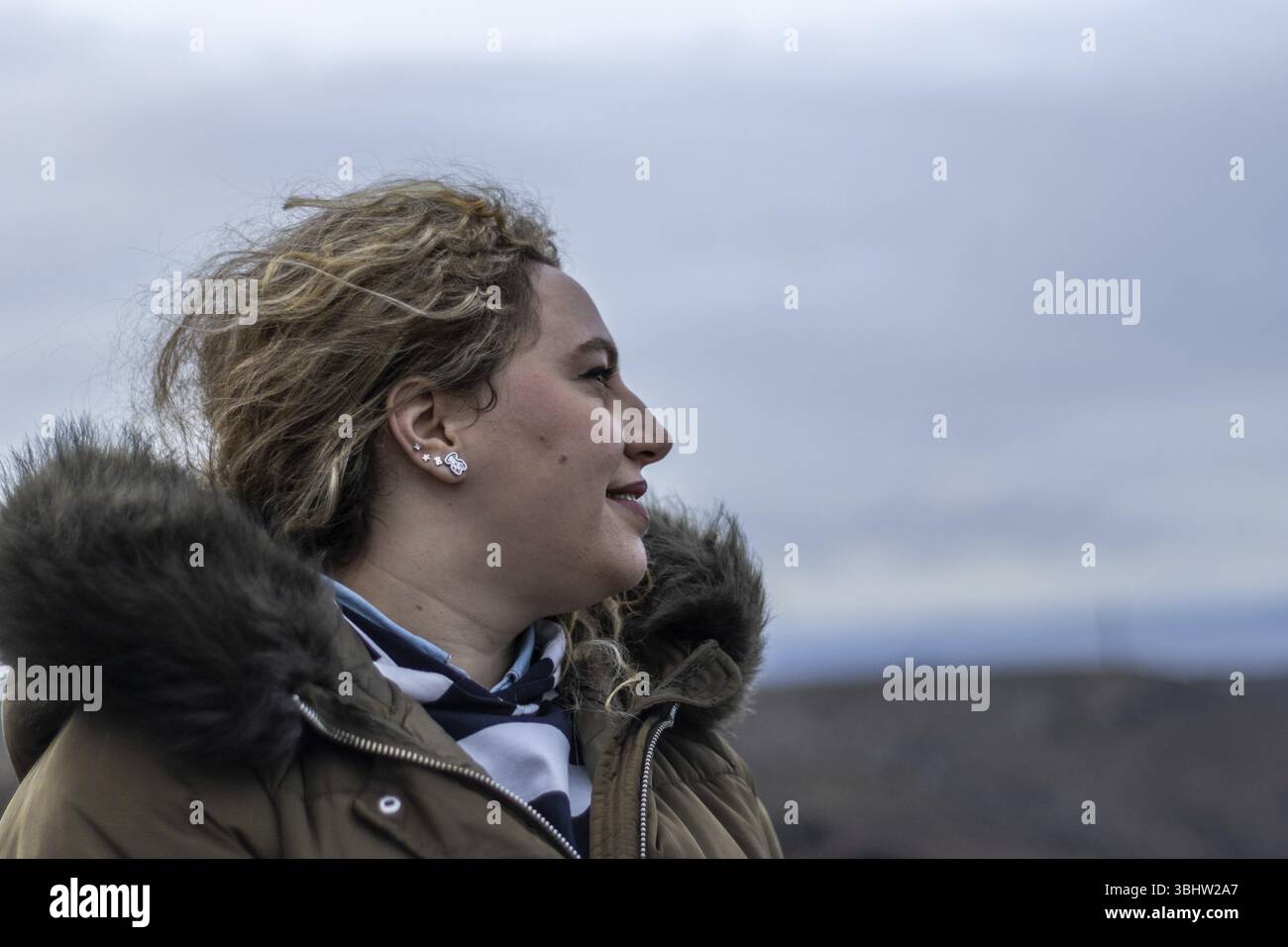 Une femme de profil un jour d'automne portant un manteau et les yeux fermés alors que le vent souffle sur son visage en plein air Banque D'Images