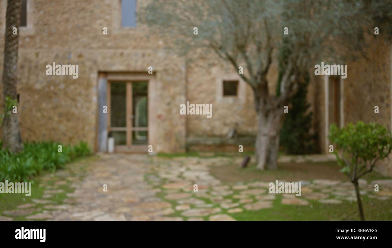 Vue floue sur une ancienne maison méditerranéenne en pierre avec un effet bokeh, avec un cadre extérieur rustique avec des arbres et de la verdure au premier plan. Banque D'Images