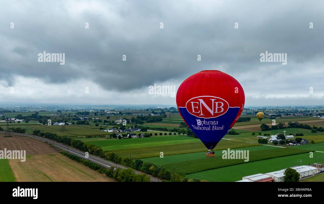 Bird in Hand, Pennsylvanie, 13 septembre 2024 - des montgolfières colorées s'élèvent au-dessus de terres agricoles luxuriantes en Pennsylvanie. La vue capture le patchwork de champs et de maisons lointaines sous un ciel couvert, mettant en valeur une atmosphère sereine. Banque D'Images