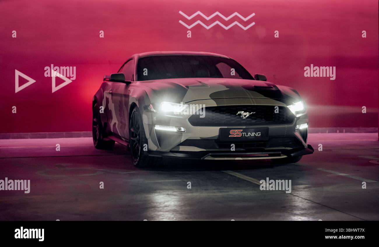 Camo beige Ford Mustang dans le garage de stationnement. Vue de trois quarts de face du poney américain garé près d'un mur marron illuminé. Banque D'Images