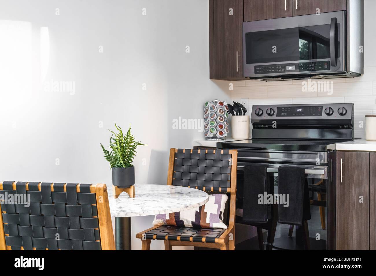 Table de cuisine, chaises tissées et appareils modernes dans un intérieur de maison de location de vacances Banque D'Images
