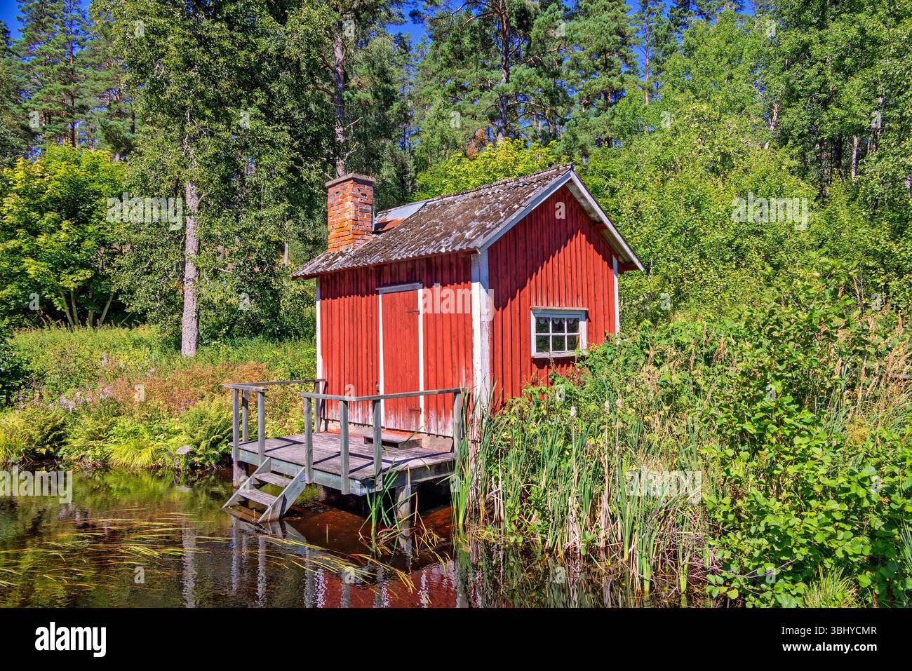 Chalet rouge avec une jetée à un lac forestier une belle journée d'été ensoleillée Banque D'Images