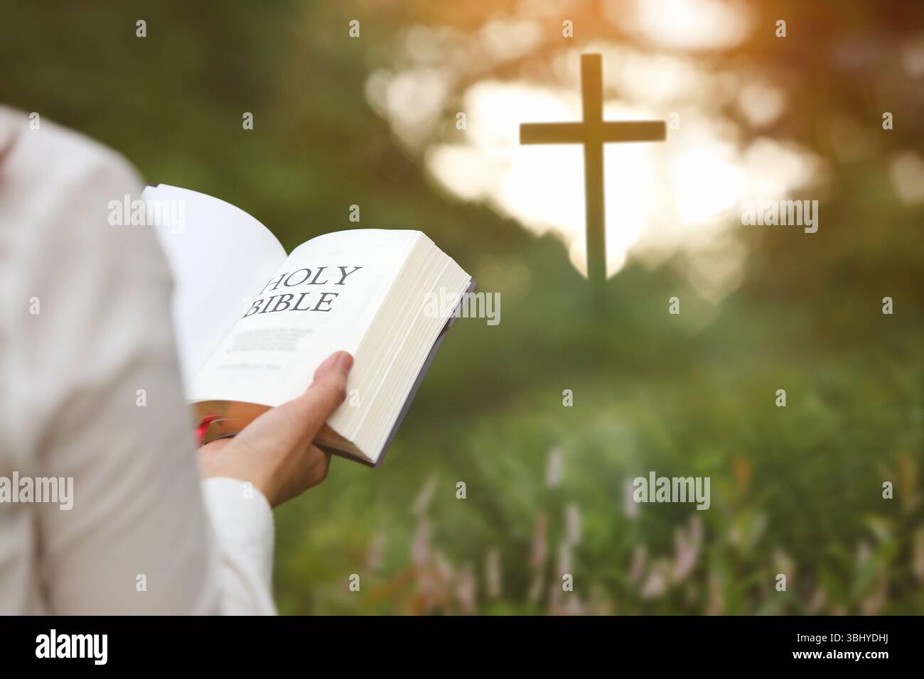 Femme chrétienne tenant la Bible et lisant la parole de Dieu dans la forêt avec la croix d'église brillamment éclairée, la foi et la croyance fond Banque D'Images