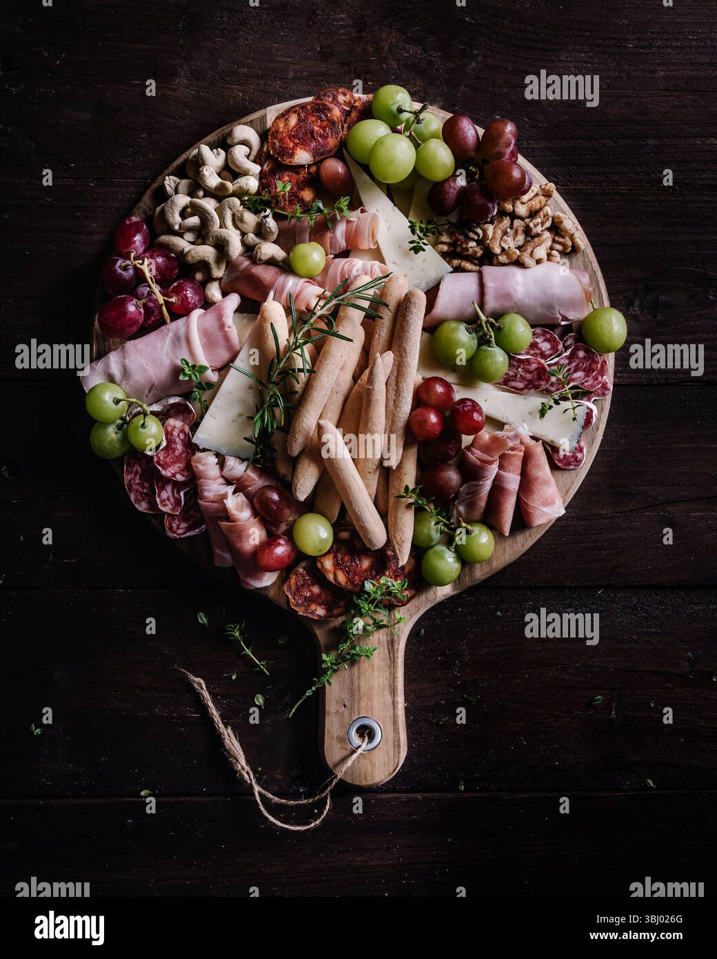Une planche de charcuterie magnifiquement agencée avec une variété de collations, y compris des charcuteries, des fromages, des raisins frais, des noix et des gressins, parfait fo Banque D'Images
