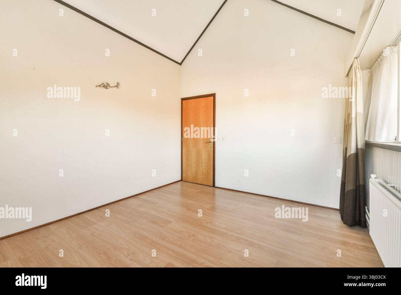 Un intérieur propre et simple avec parquet, une porte et de grandes fenêtres permettant à la lumière naturelle d'inonder la pièce, créant une atmosphère sereine Banque D'Images