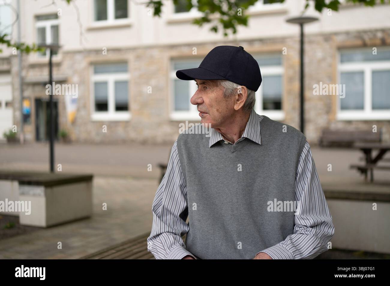 Homme âgé dans le gilet tricoté casquette de baseball et chemise assis sur le banc sur fond de rue flou. Concept de vieillesse active Banque D'Images