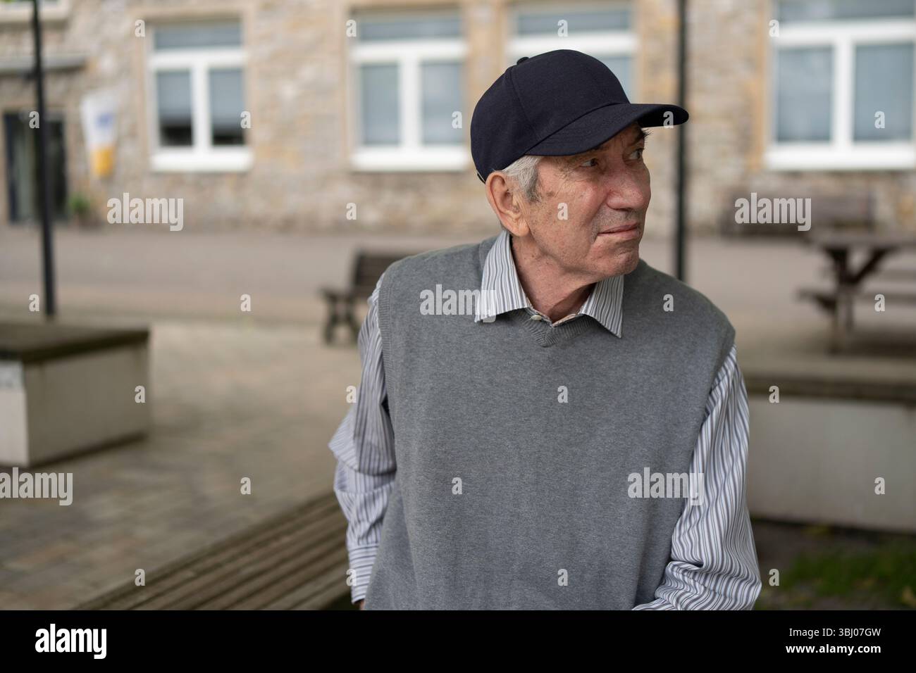 Homme âgé dans le gilet tricoté casquette de baseball et chemise assis sur le banc sur fond de rue flou. Concept de vieillesse active Banque D'Images