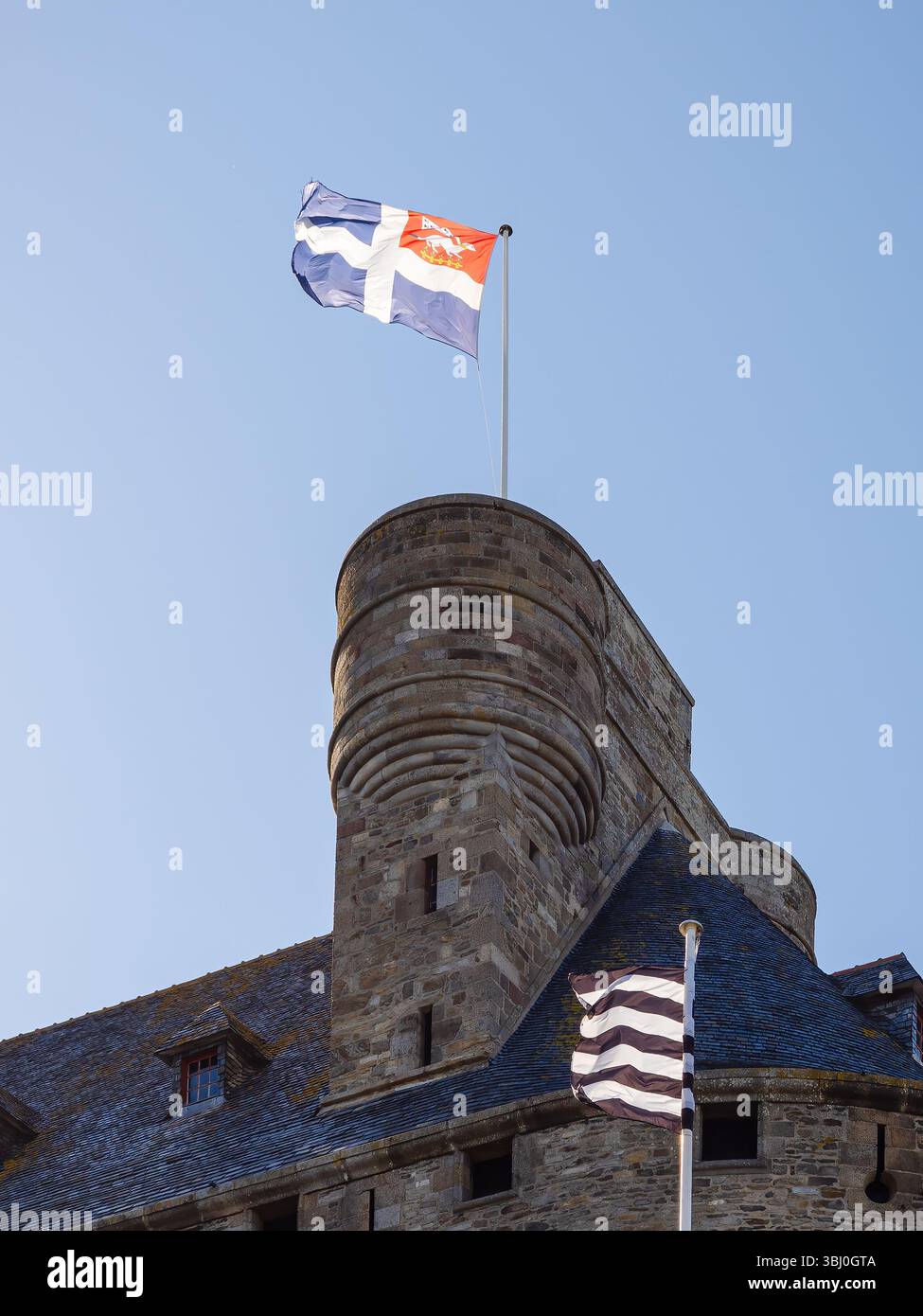 Tour de la mairie de Saint-Malo avec le drapeau de la ville et le drapeau de Bretagne agitant au vent, architecture traditionnelle en pierre sous ciel bleu en Bretagne, France Banque D'Images