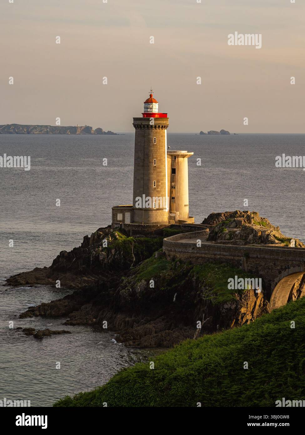 Vue verticale du phare du petit Minou sur la côte du Finistère, Bretagne, France, éclairé par la lumière dorée du coucher de soleil avec des rochers spectaculaires et un océan calme. Banque D'Images