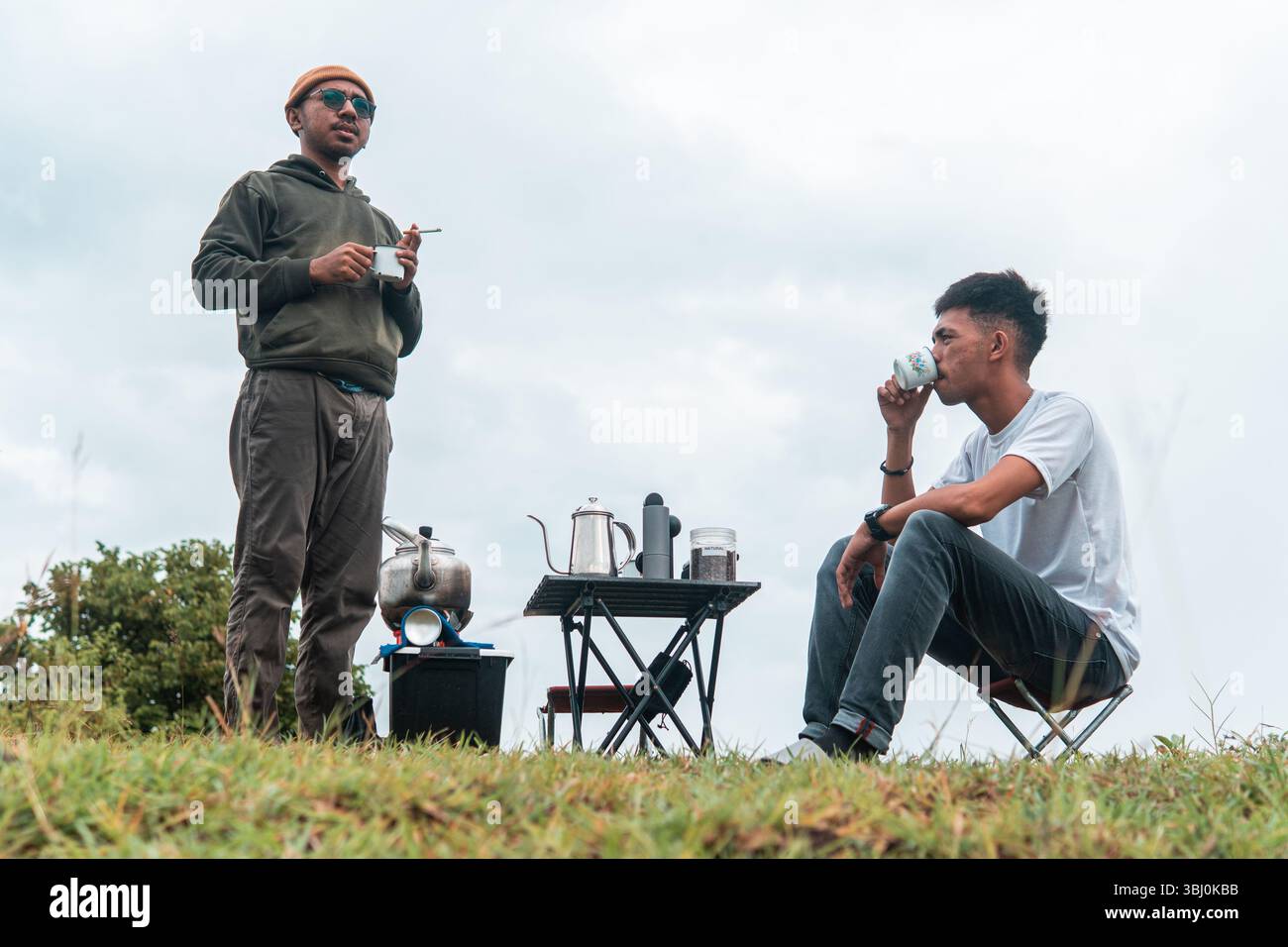 Deux hommes dans un cadre extérieur détendu tout en préparant le café. Un moment cosy de camping, de liaison et de profiter de la nature. Banque D'Images