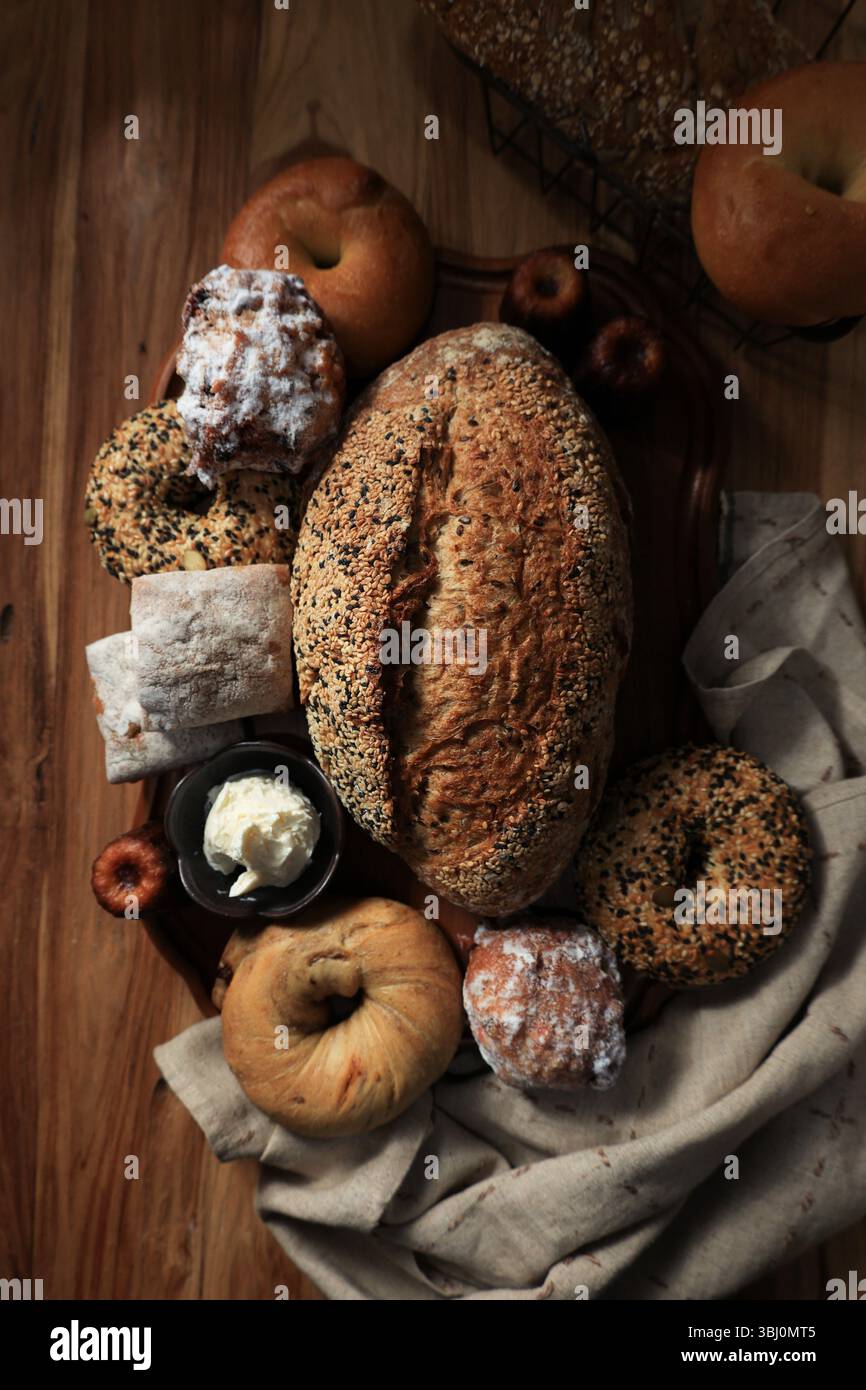Multi Seed Sourdough avec un autre produit de boulangerie sur la table en bois. Bagels, pain, Ciabatta, Canele et Oliebollen avec pâte à tartiner au fromage à la crème Banque D'Images