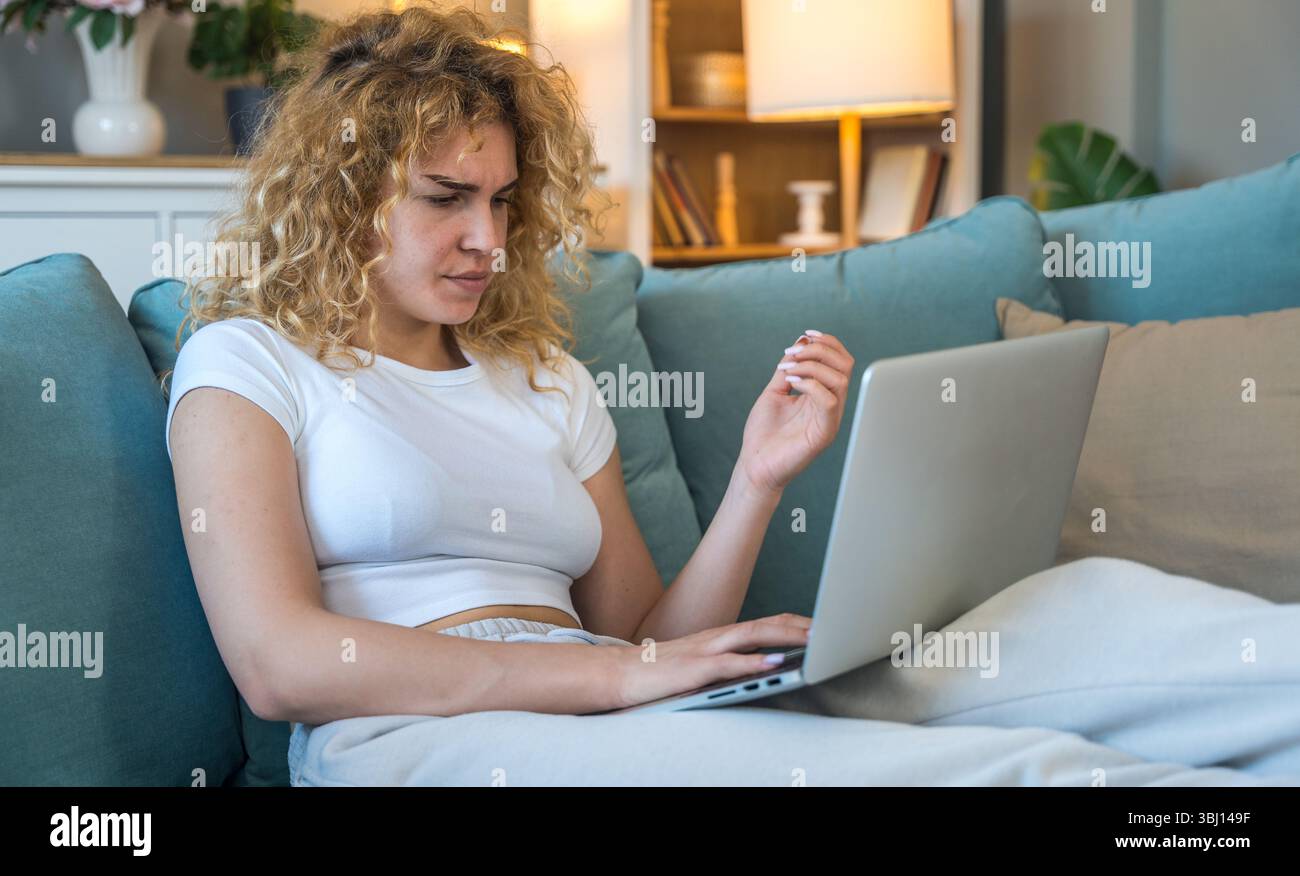 Jeune femme travaillant à la maison sur ordinateur portable éprouvant des problèmes techniques tels que la déconnexion d'Internet, un problème informatique ou une erreur système, frustrée et Banque D'Images