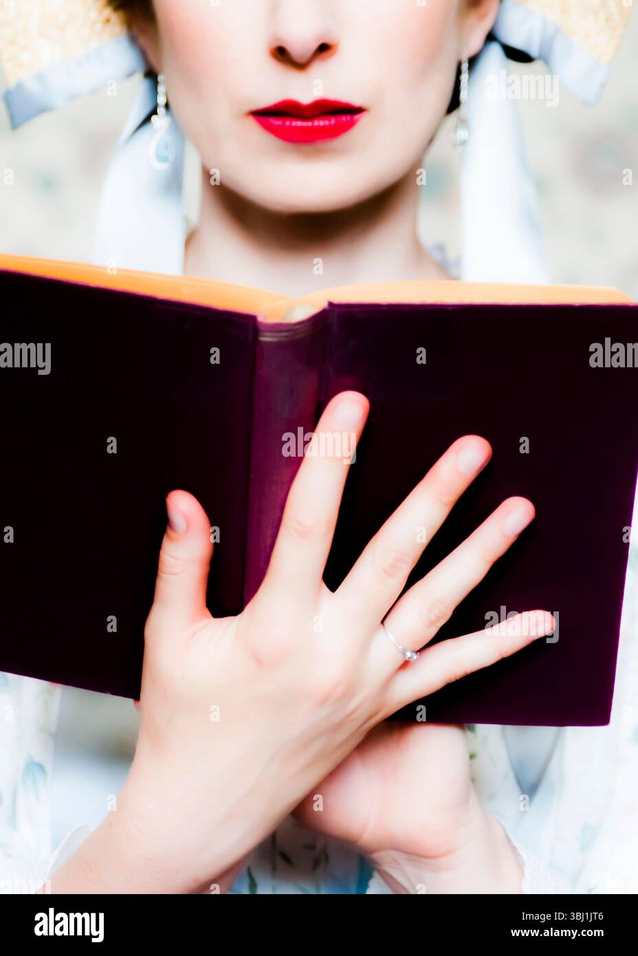 Une femme avec du rouge à lèvres rouge et un chapeau de paille tient un livre. Banque D'Images