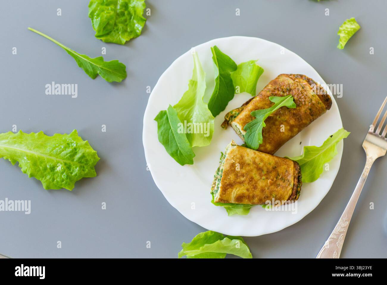 Rouleau d'oeufs sain avec des verts sur une assiette blanche. Banque D'Images