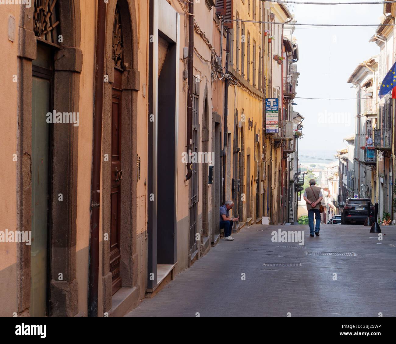 Rue escarpée dans le centre historique de Montefiascone que les hommes marchent et s'assoient sur les marches. Italie. 12 juin 2025. Banque D'Images