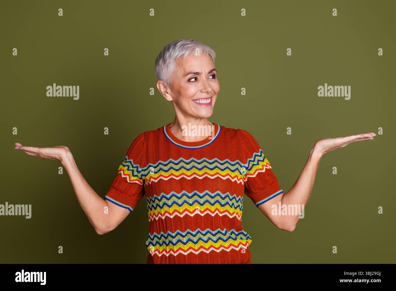 Femme âgée souriante avec les cheveux courts montrant un geste de paume ouverte sur un fond kaki Banque D'Images