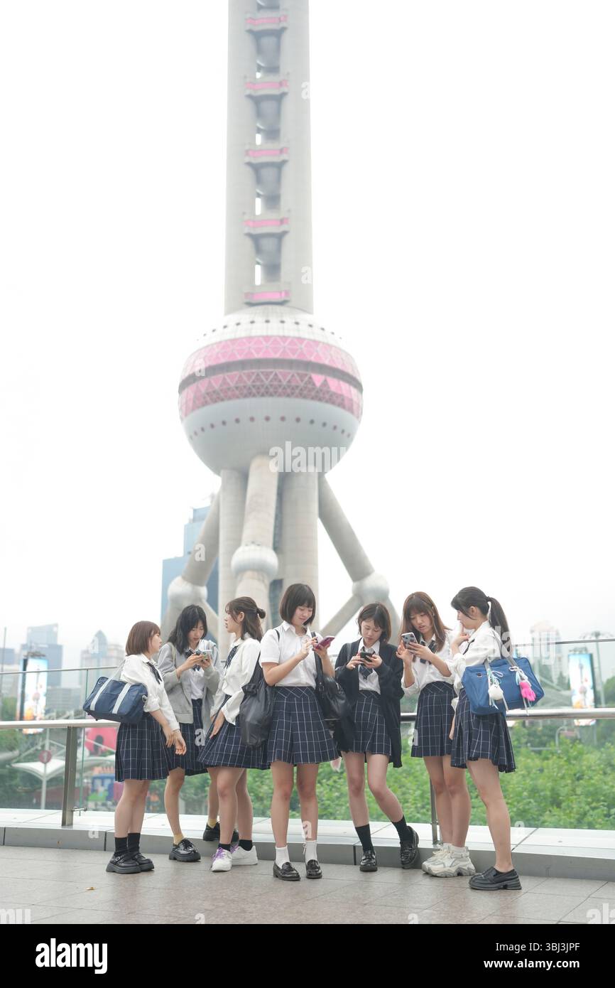 Au début de l'été à Shanghai, près du Bund, des lycéennes japonaises en uniforme se rassemblent devant la Tour de la Perle orientale, leur présence s'ajoutant Banque D'Images