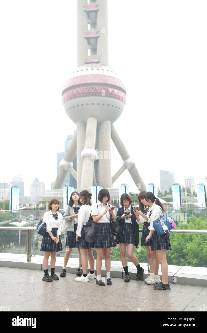 Au début de l'été à Shanghai, près du Bund, des lycéennes japonaises en uniforme se rassemblent devant la Tour de la Perle orientale, leur présence s'ajoutant Banque D'Images