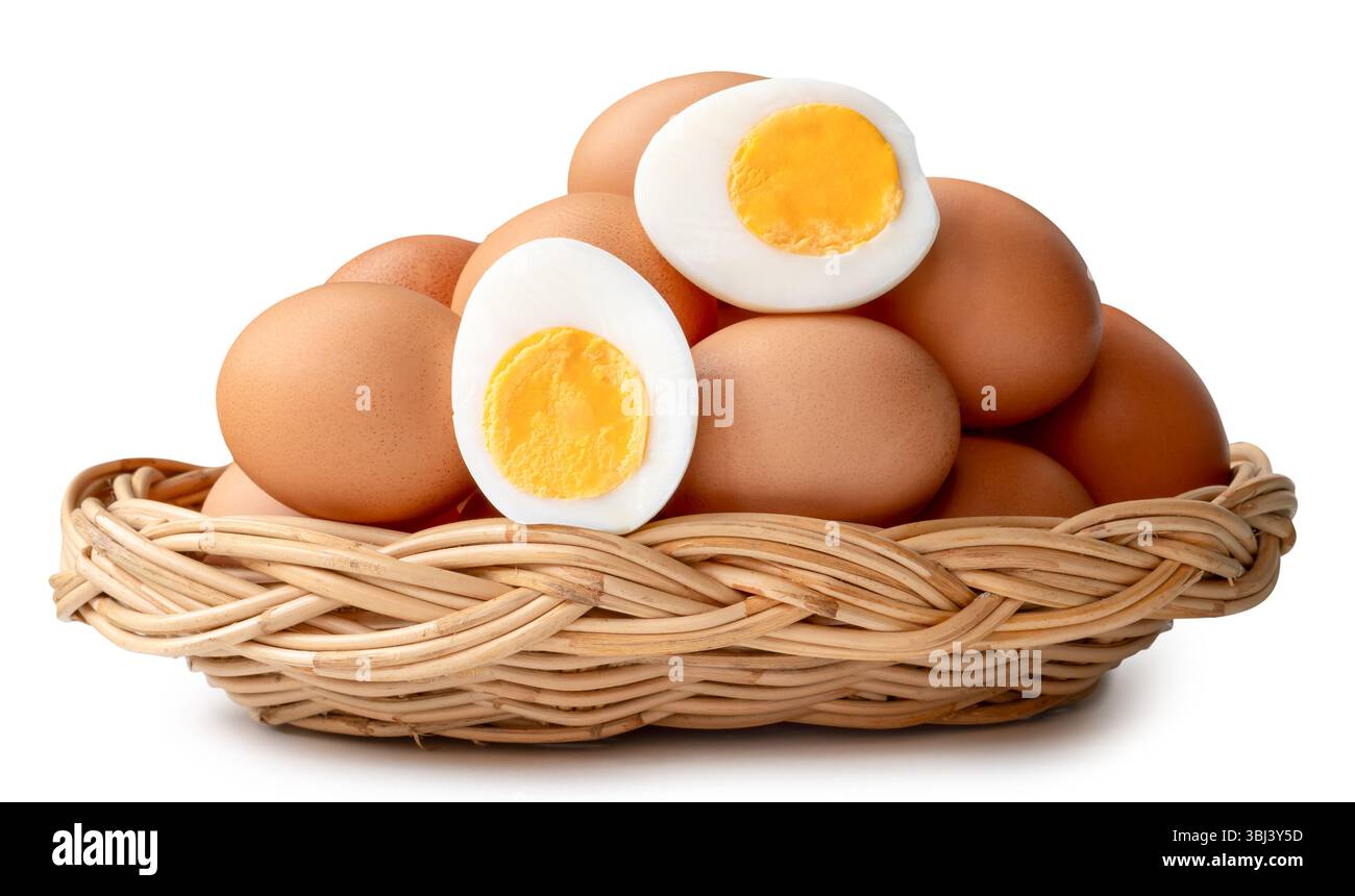 Un grand groupe d'œufs de poule brune crue et d'œufs cuits ou durs pelés avec jaune d'œuf en deux moitiés en pile dans un panier en osier est isolé sur blanc. Banque D'Images