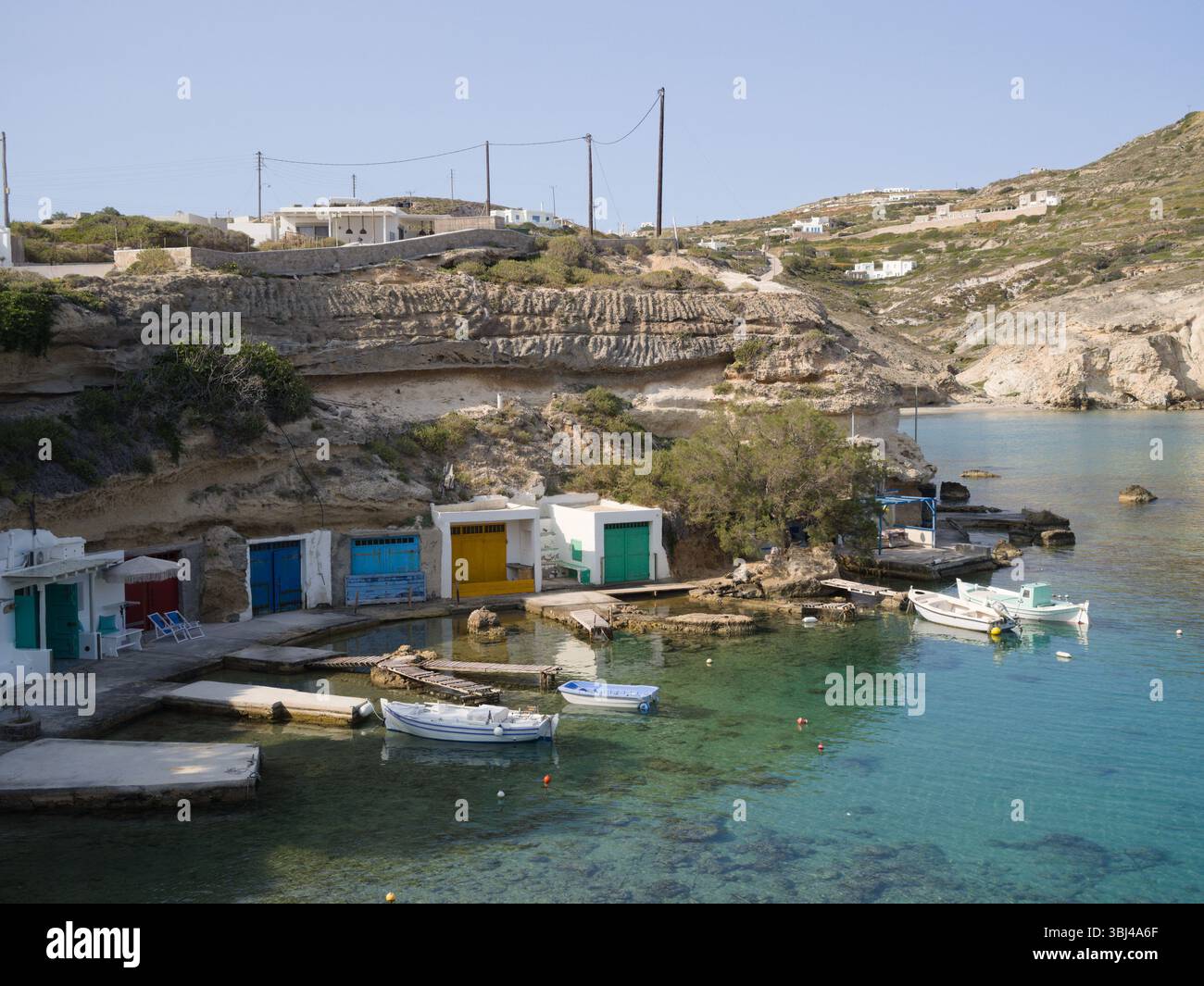 La lumière du soleil illumine les falaises blanches de Mandrakia et les cabanes de pêche vibrantes au-dessus de l'eau turquoise lors d'une journée d'été calme à Milos, en Grèce. Banque D'Images