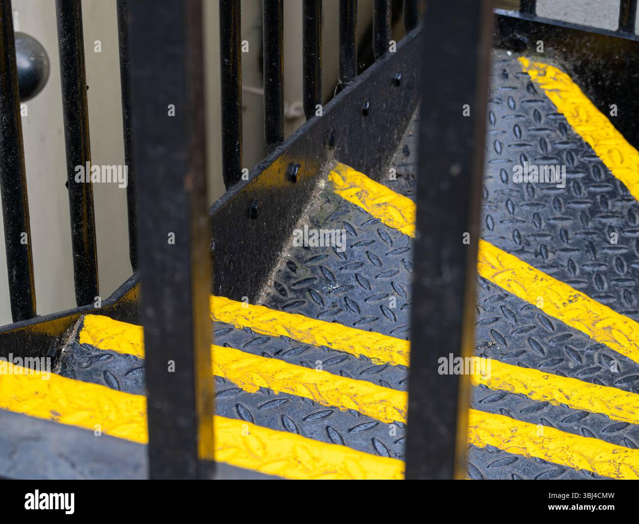 Une vue rapprochée d'un escalier avec des bandes de sécurité jaunes et des rampes métalliques. Les escaliers ont une surface texturée, améliorant l'adhérence et la sécurité. Industria Banque D'Images