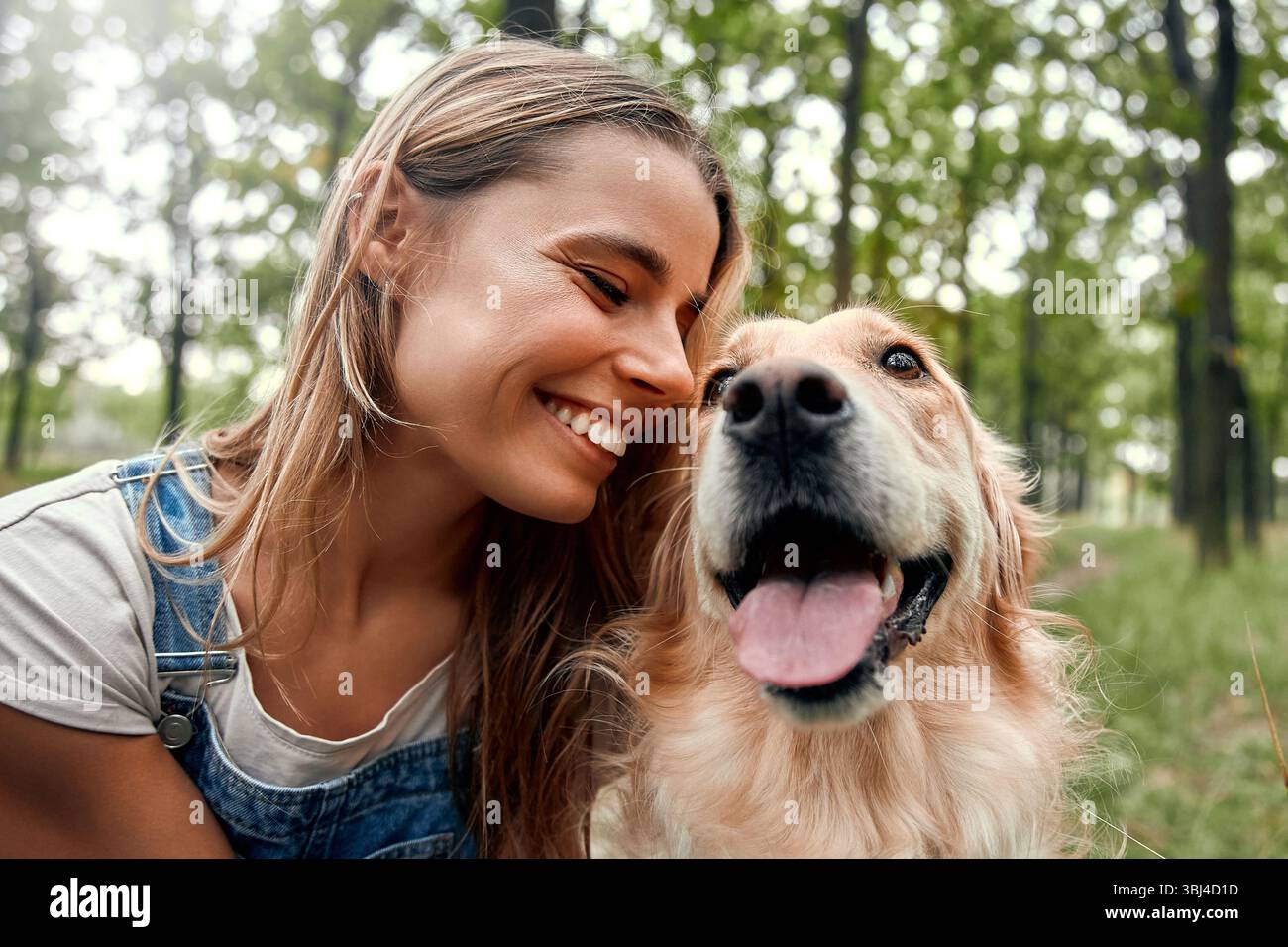 Dans un parc serein, une jeune femme joyeuse rayonne de bonheur tandis que son Golden retriever ludique à côté d'elle incarne la véritable essence de la compagnie, la joie Banque D'Images