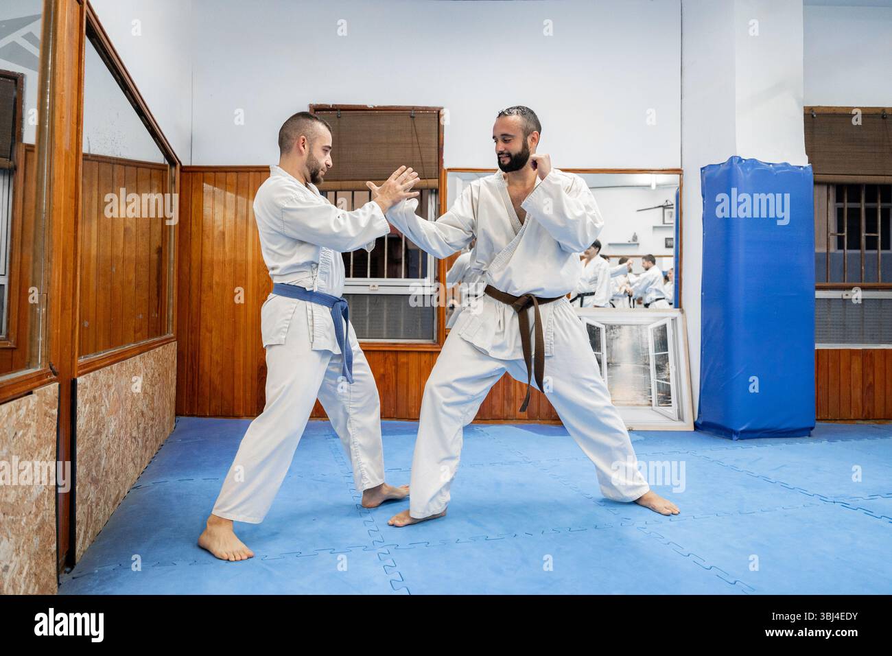 Deux hommes pratiquant le karaté dans un dojo, portant des kimonos blancs et des ceintures, effectuant un mouvement défensif Banque D'Images