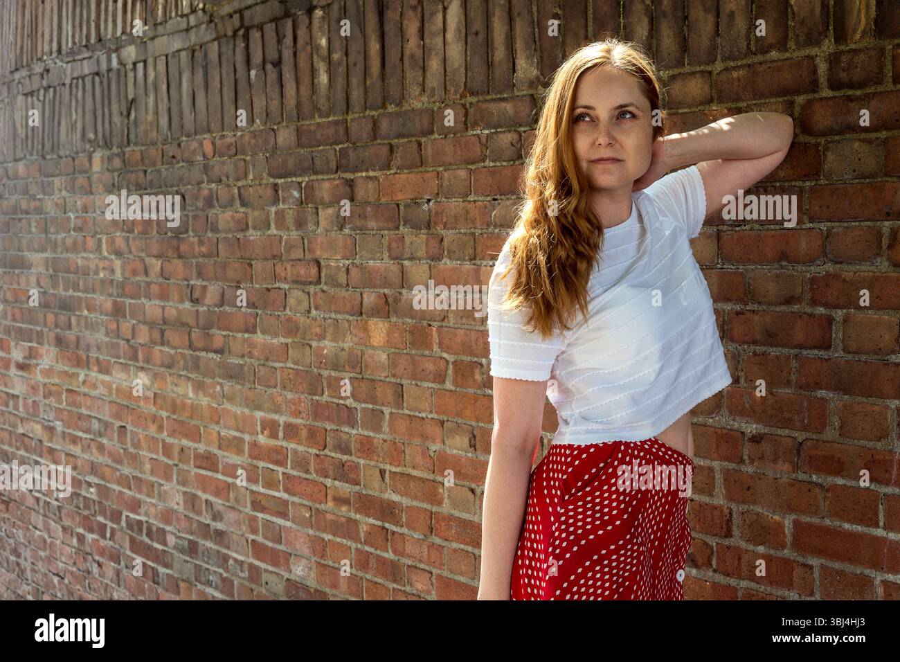 Jeune femme réfléchie à côté d'un mur de briques, portrait extérieur Banque D'Images