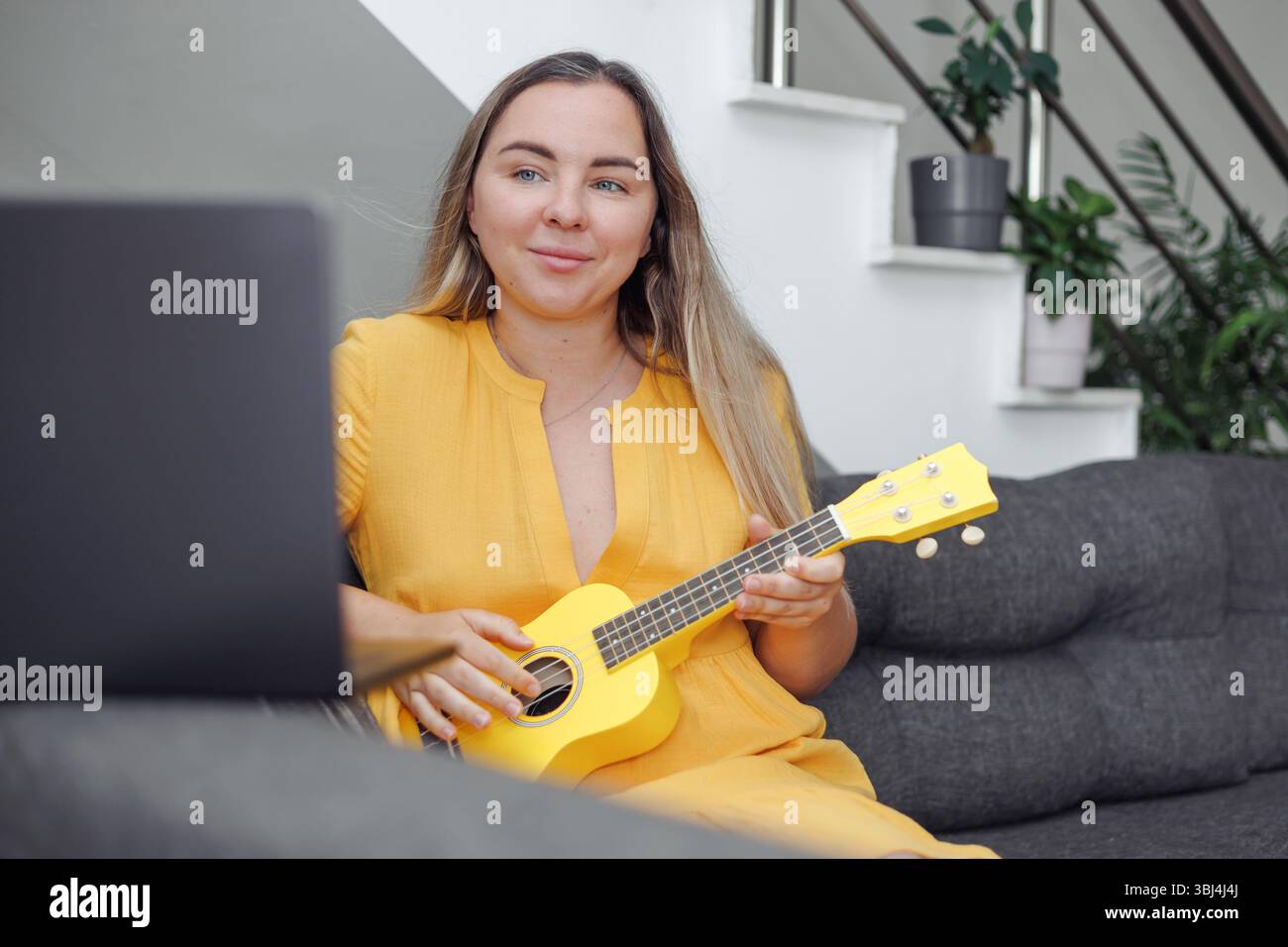 Femme joue du ukulélé jaune, classe de musique en ligne à la maison Banque D'Images