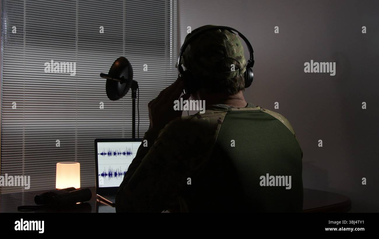 Un officier militaire en uniforme de camouflage conduit une audition dans un environnement isolé. Un équipement audio professionnel est utilisé - écouteurs, microphon Banque D'Images