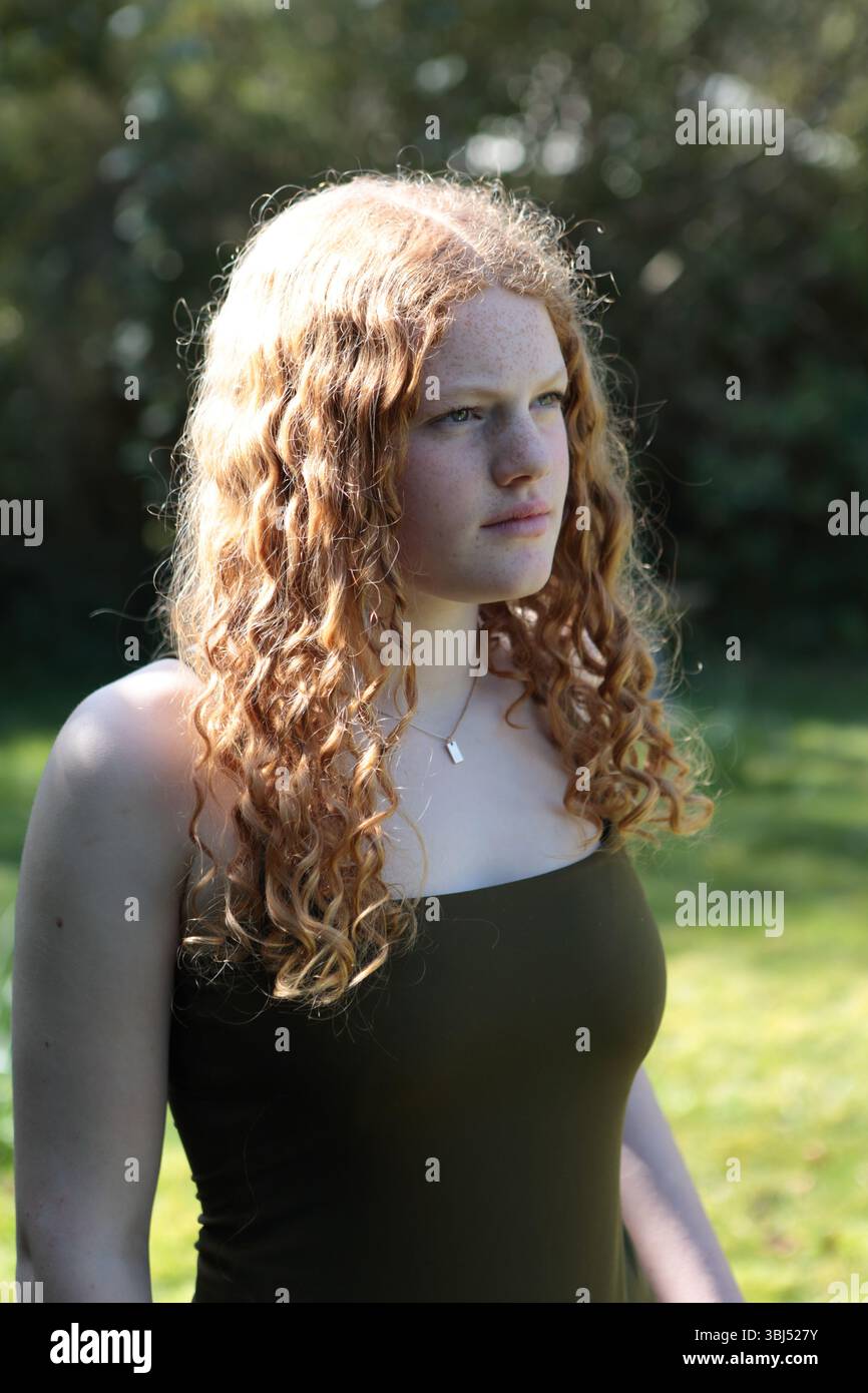 Portrait d'adolescente cheveux bouclés de gingembre dans le jardin rétro-éclairé avec la lumière du soleil Banque D'Images