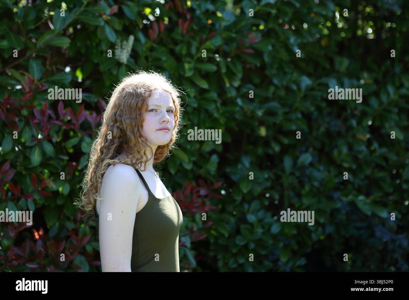 Portrait d'adolescente cheveux bouclés de gingembre dans le jardin rétro-éclairé avec la lumière du soleil Banque D'Images