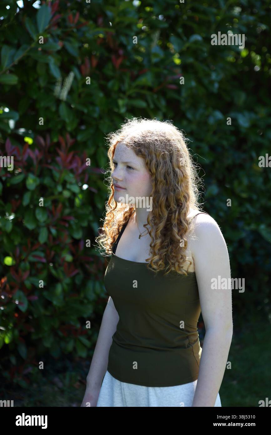Portrait d'adolescente cheveux bouclés de gingembre dans le jardin rétro-éclairé avec la lumière du soleil Banque D'Images