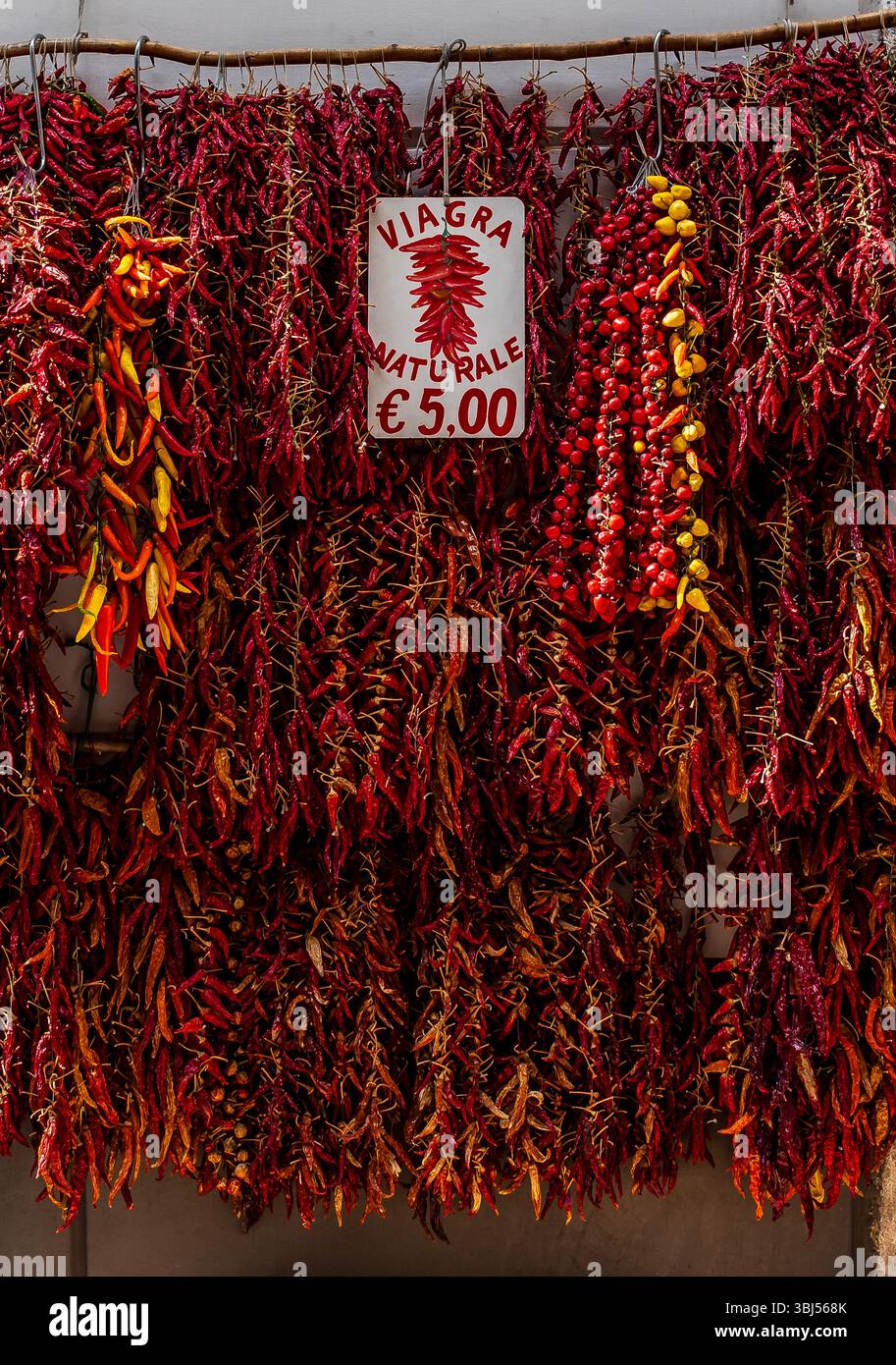 Un panneau de rue humoristique indiquant « Viagra naturel » se trouve au-dessus d'une exposition extérieure de piments italiens rouges vifs à vendre dans un marché local animé. Banque D'Images