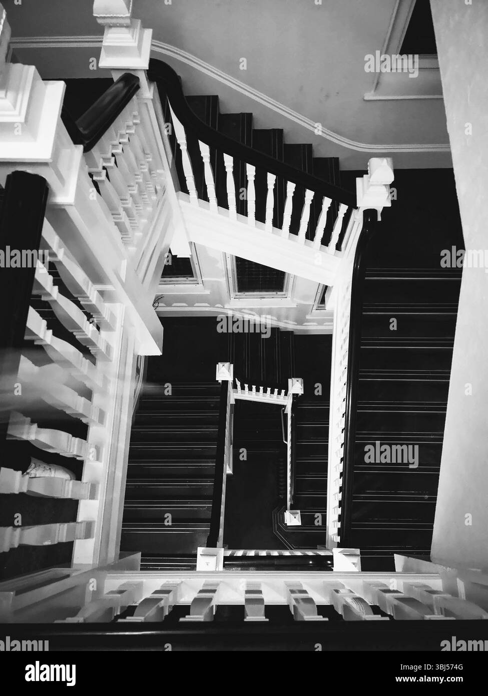 Spectaculaire photo en noir et blanc d'un escalier en colimaçon orné, vu de haut en bas, avec des ombres audacieuses et élégantes bannières traditionnelles. - Image de stock capturée avec un smartphone