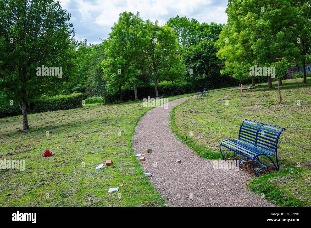 Une scène de parc agréable avec un sentier et des bancs, gâtés par la litière dispersée d'emballage de boisson sur le sol Banque D'Images