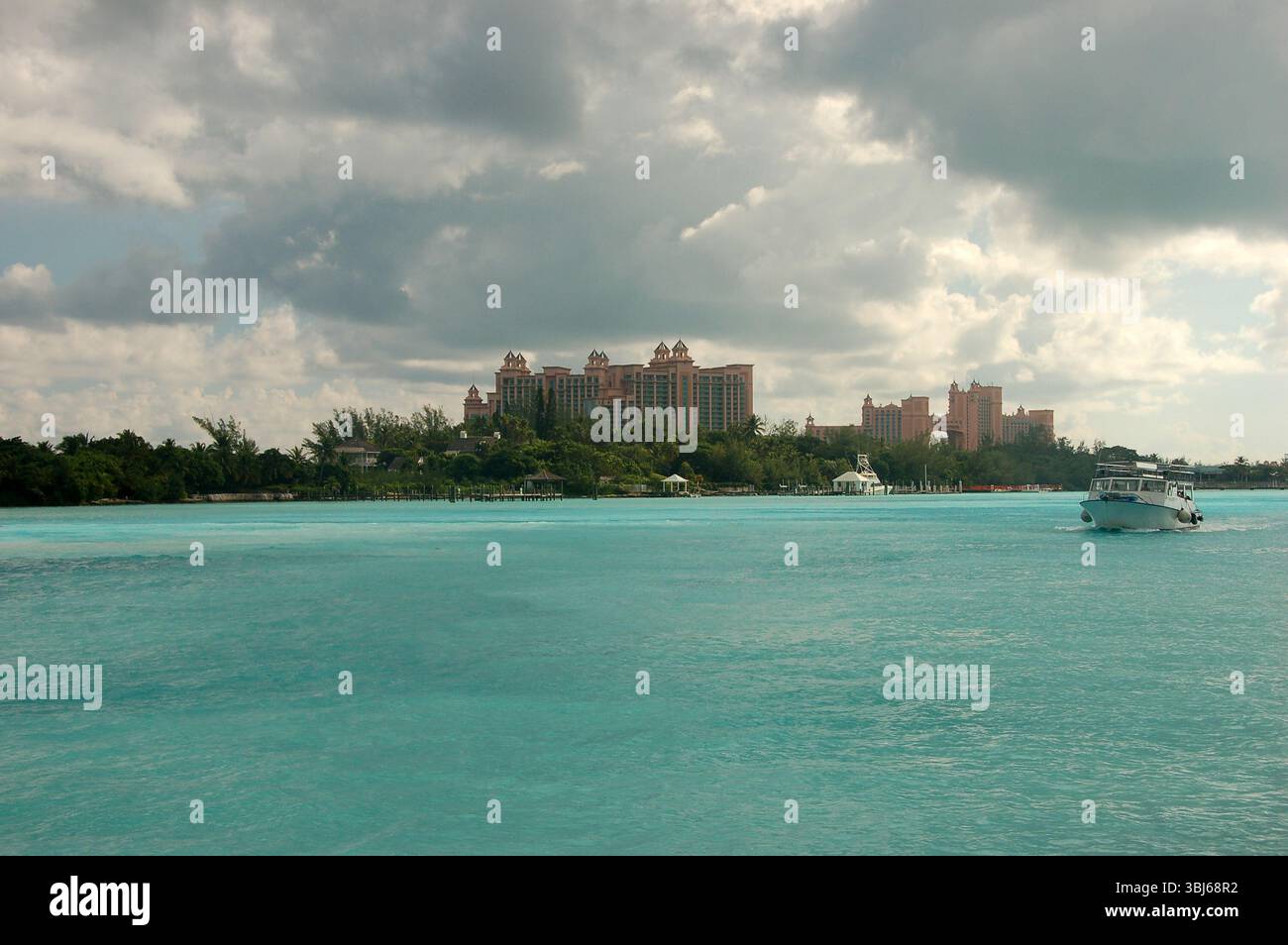 Un bateau glisse sur les eaux turquoises calmes près de Paradise Island aux Bahamas, avec l'emblématique Atlantis Resort debout sous un ciel nuageux Banque D'Images